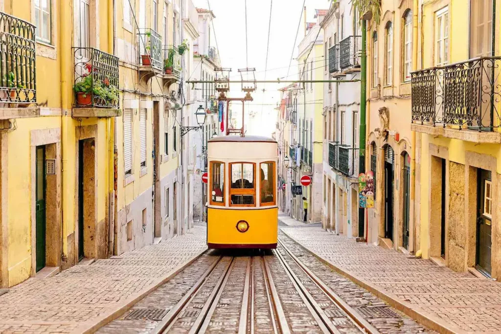 A classic yellow tram glides through a narrow, sunlit street in Lisbon surrounded by colorful buildings